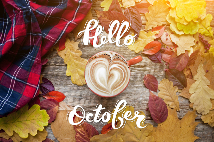 a mug with coffee latte on a table with autumn leaves and caption "hello october"