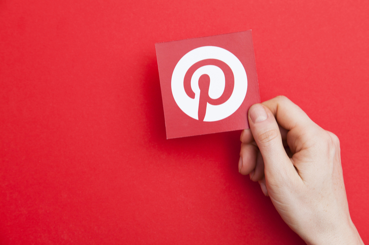 Hand holding up the Pinterest symbol. Red background elevates the logo