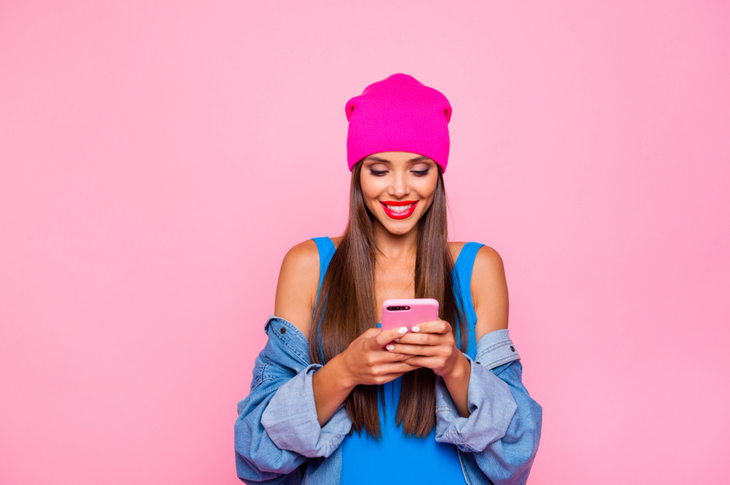 When to choose micro-influencers : An influencer posting a picture on Instagram. Inluencer wearing trendy clothes with a pink cap and pink phone