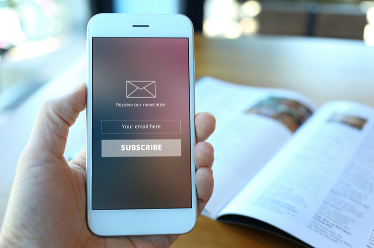 Email Newsletters Concept : Hand holding smartphone with receive newsletter form screen on cafe background